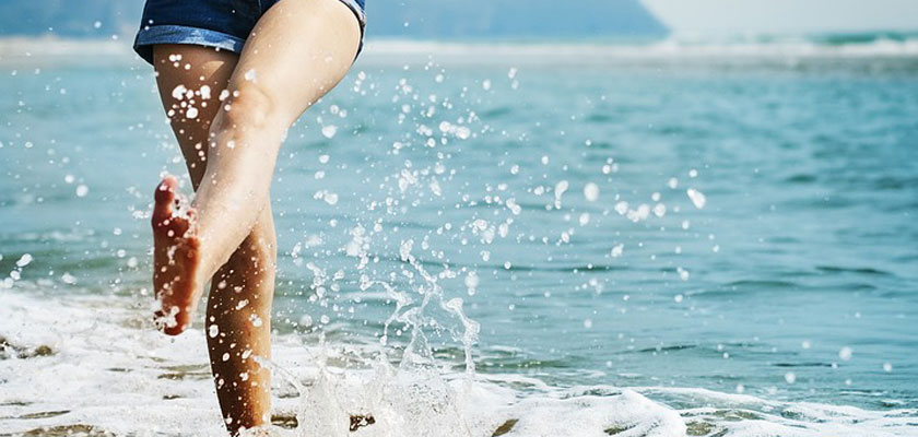 Las piernas de una chica que se ha hecho la depilación láser en verano chapoteando con el agua de la playa